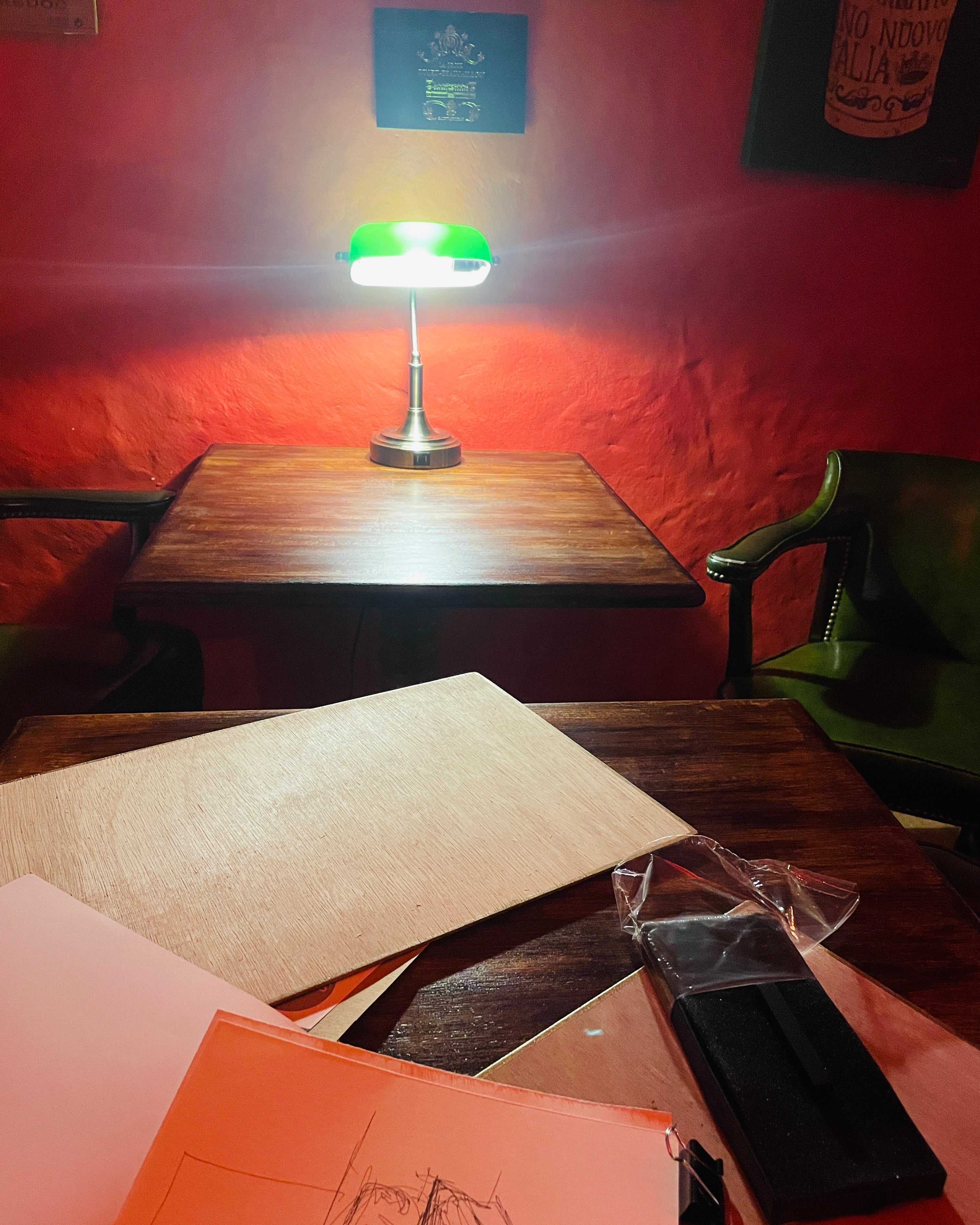 Small wooden table with a lamp against a red wall, surrounded by books and papers.